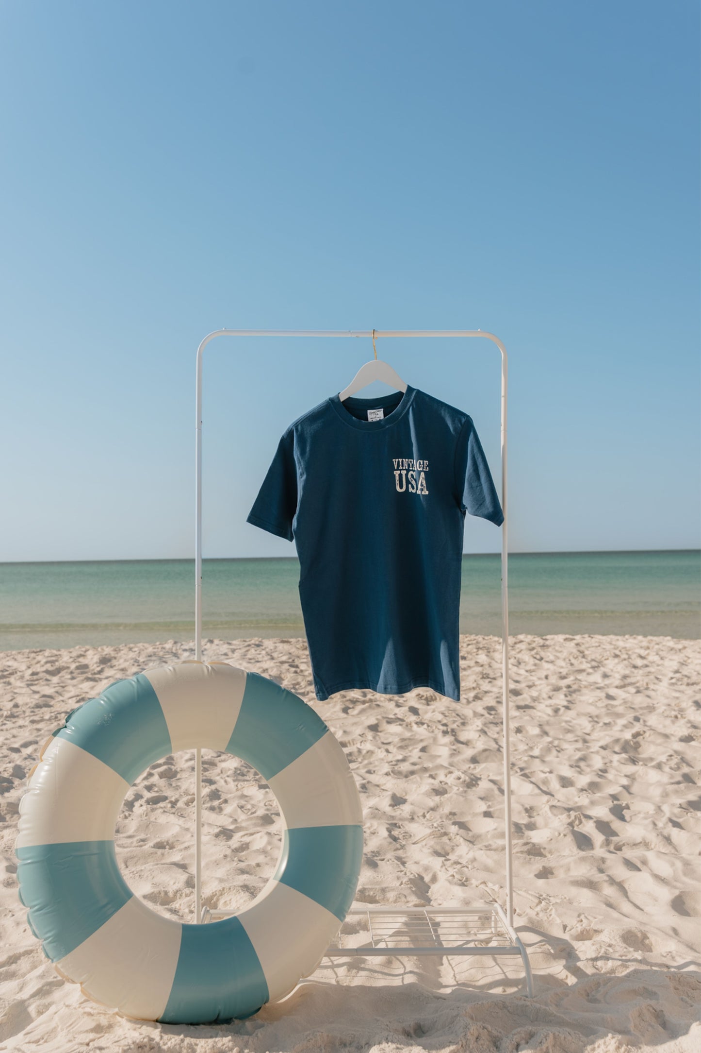 Navy blue t-shirt with 'USA' text on a white stand against a beach backdrop