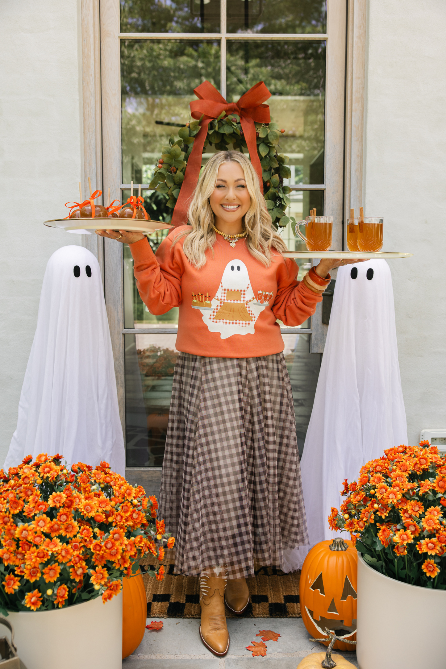 Woman in Halloween-themed outfit with ghost decorations and pumpkins.