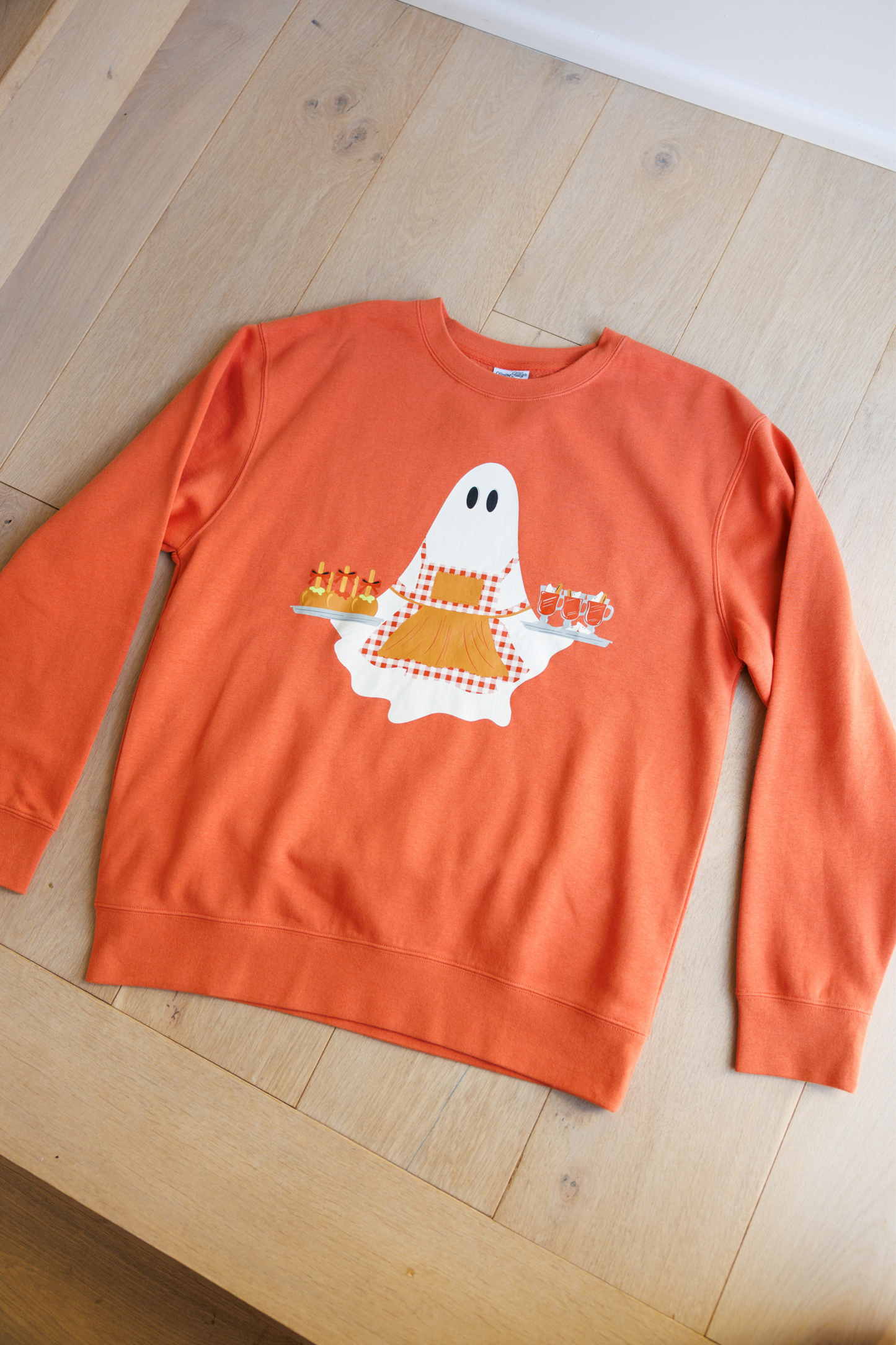 Orange sweatshirt with a ghost design on a wooden floor