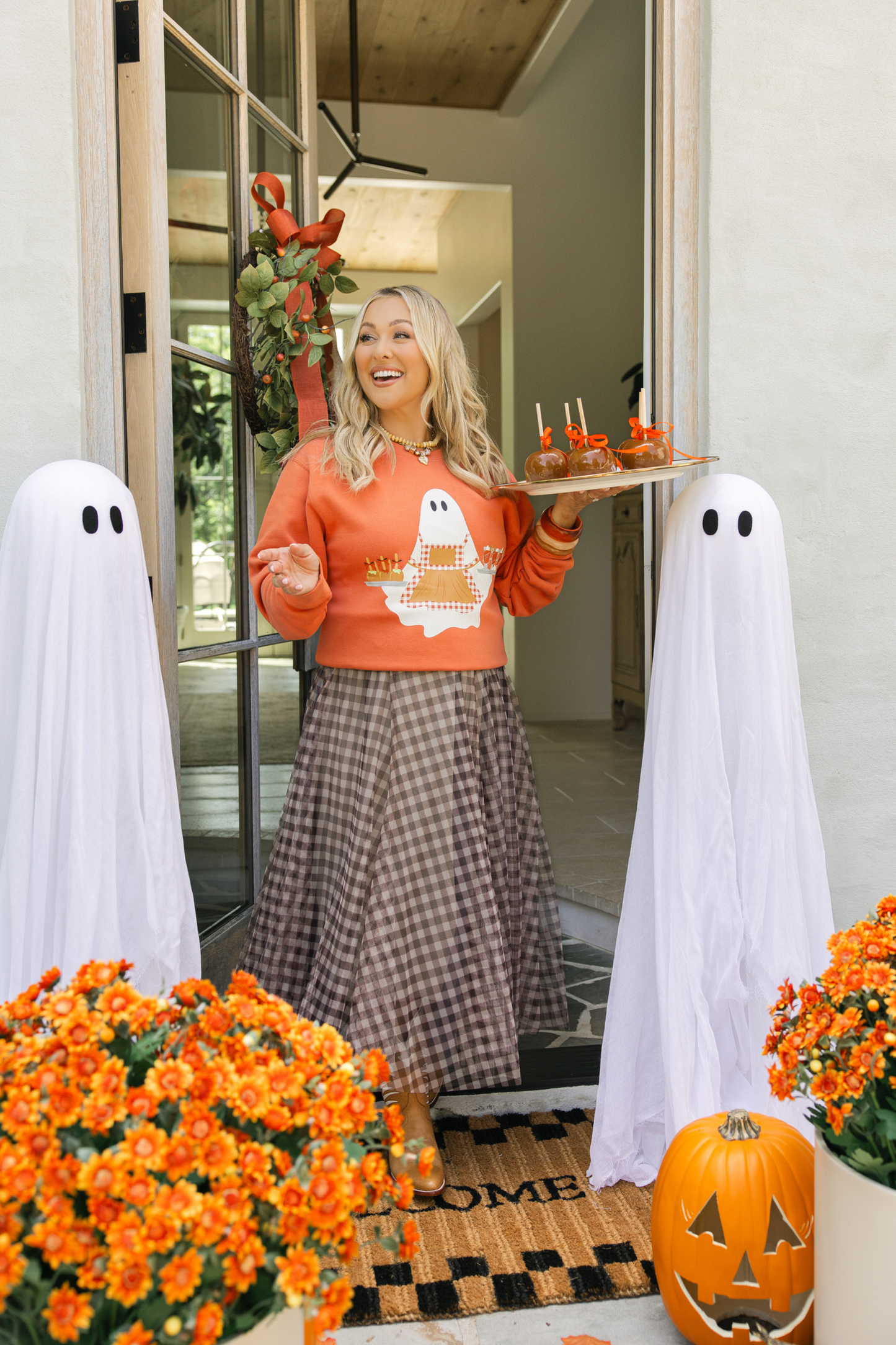 Woman in Halloween-themed outfit with ghosts and pumpkins on a decorated porch.