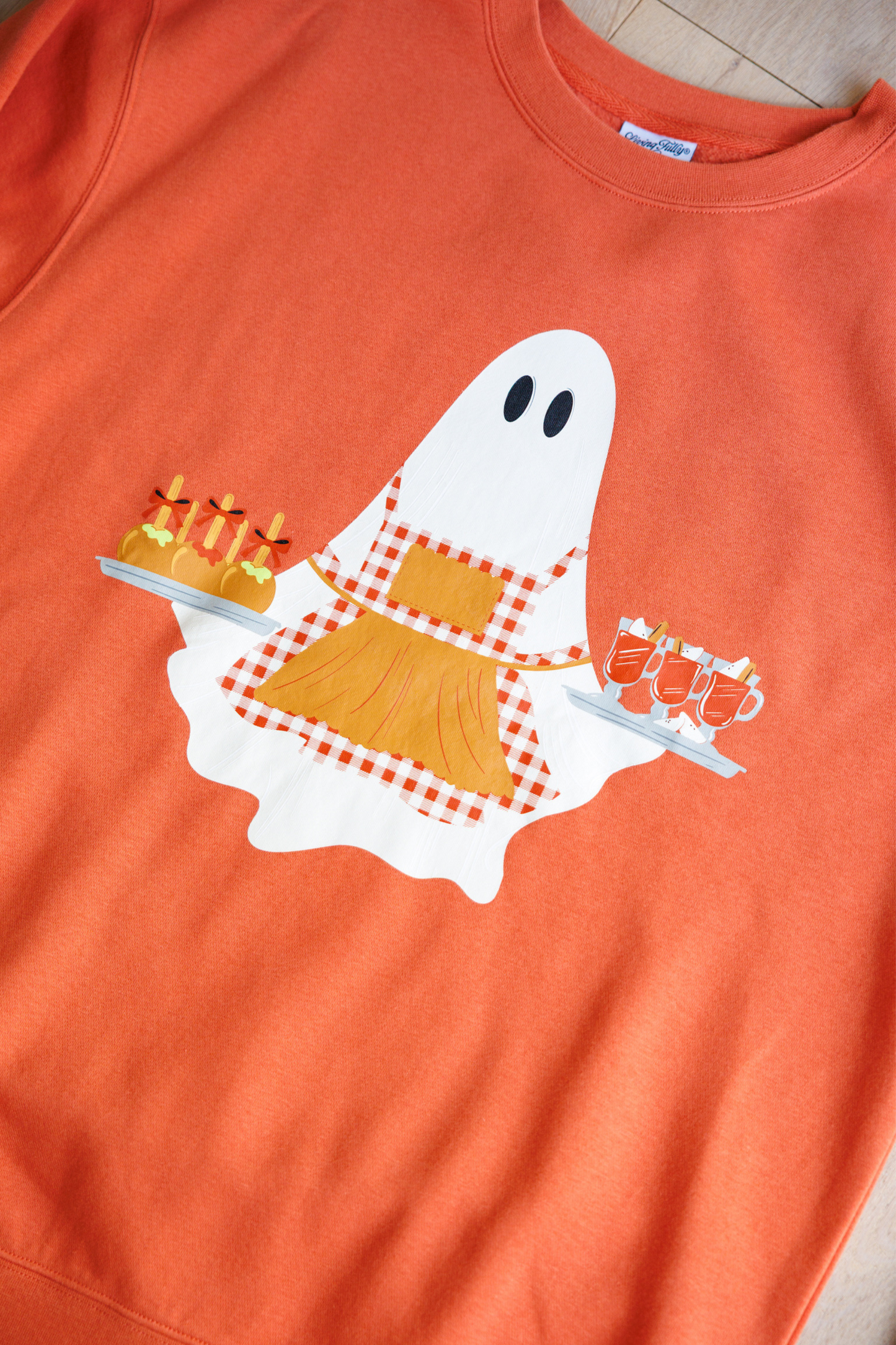Spiced orange sweatshirt with a ghost holding candy corn design on a plain background