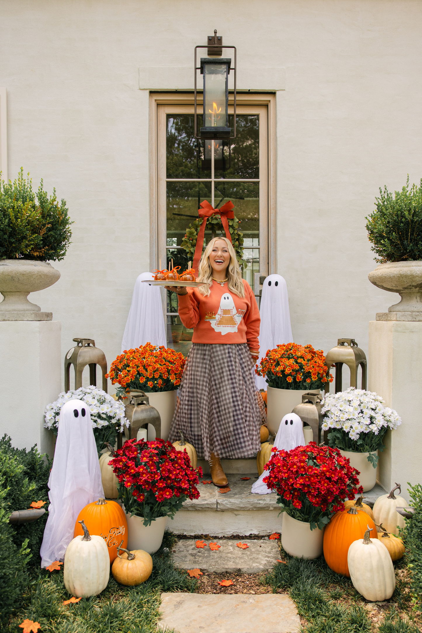 Woman in a decorated front porch with Halloween decorations, including pumpkins and flowers.