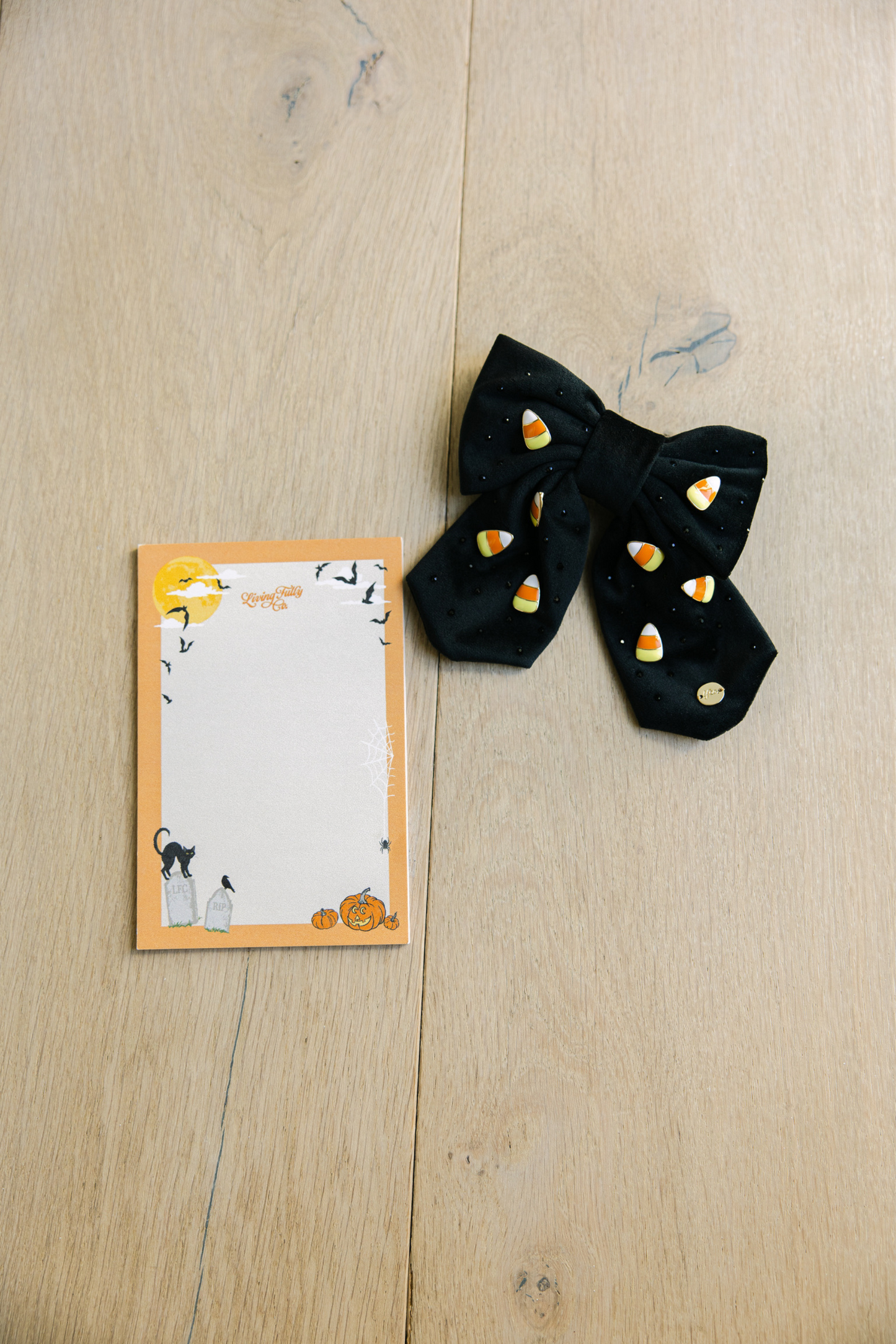 Black hair bow with candy corn design next to a Halloween-themed notepad on a wooden surface.