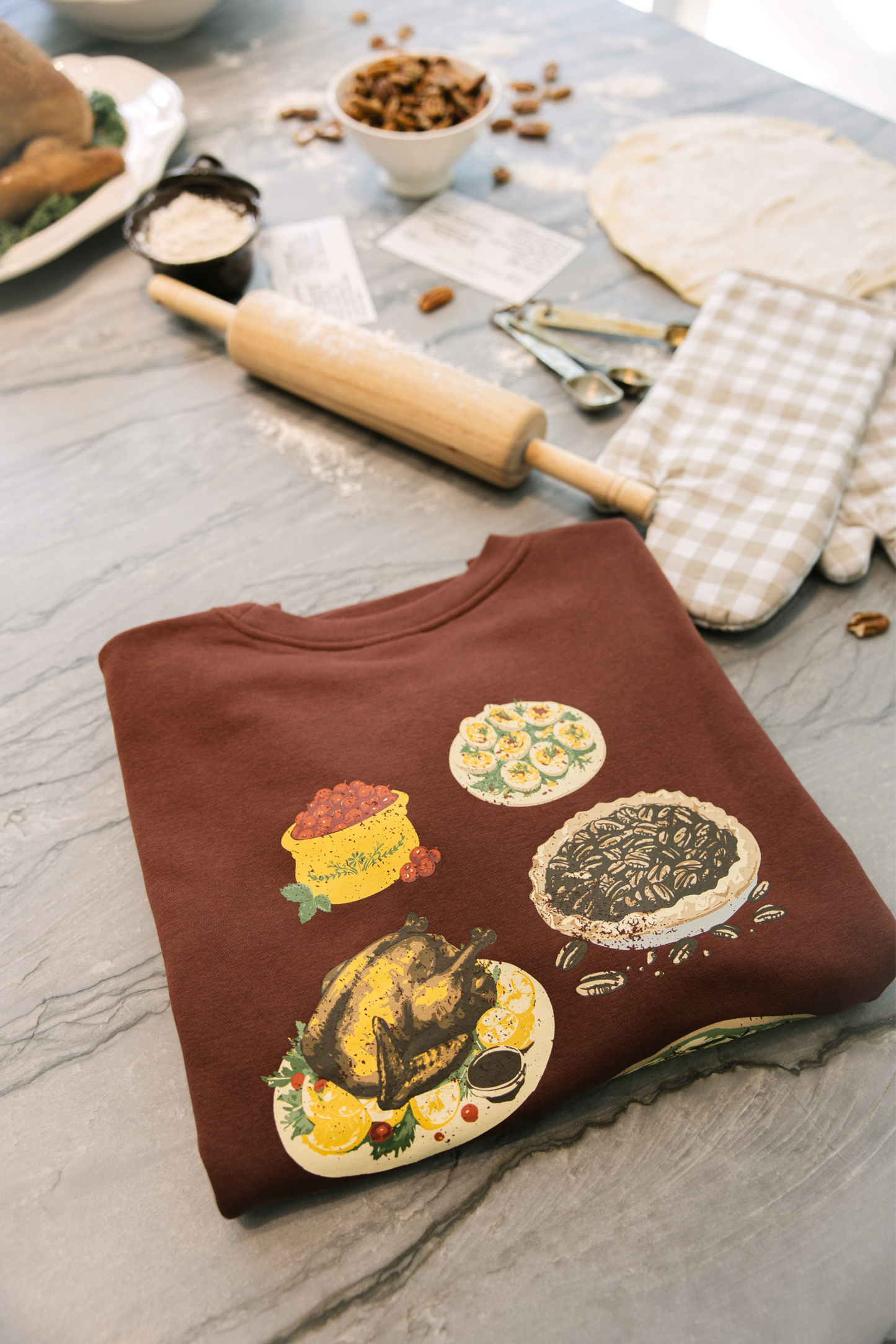 Brown sweatshirt with food-themed designs on a kitchen counter with baking tools.