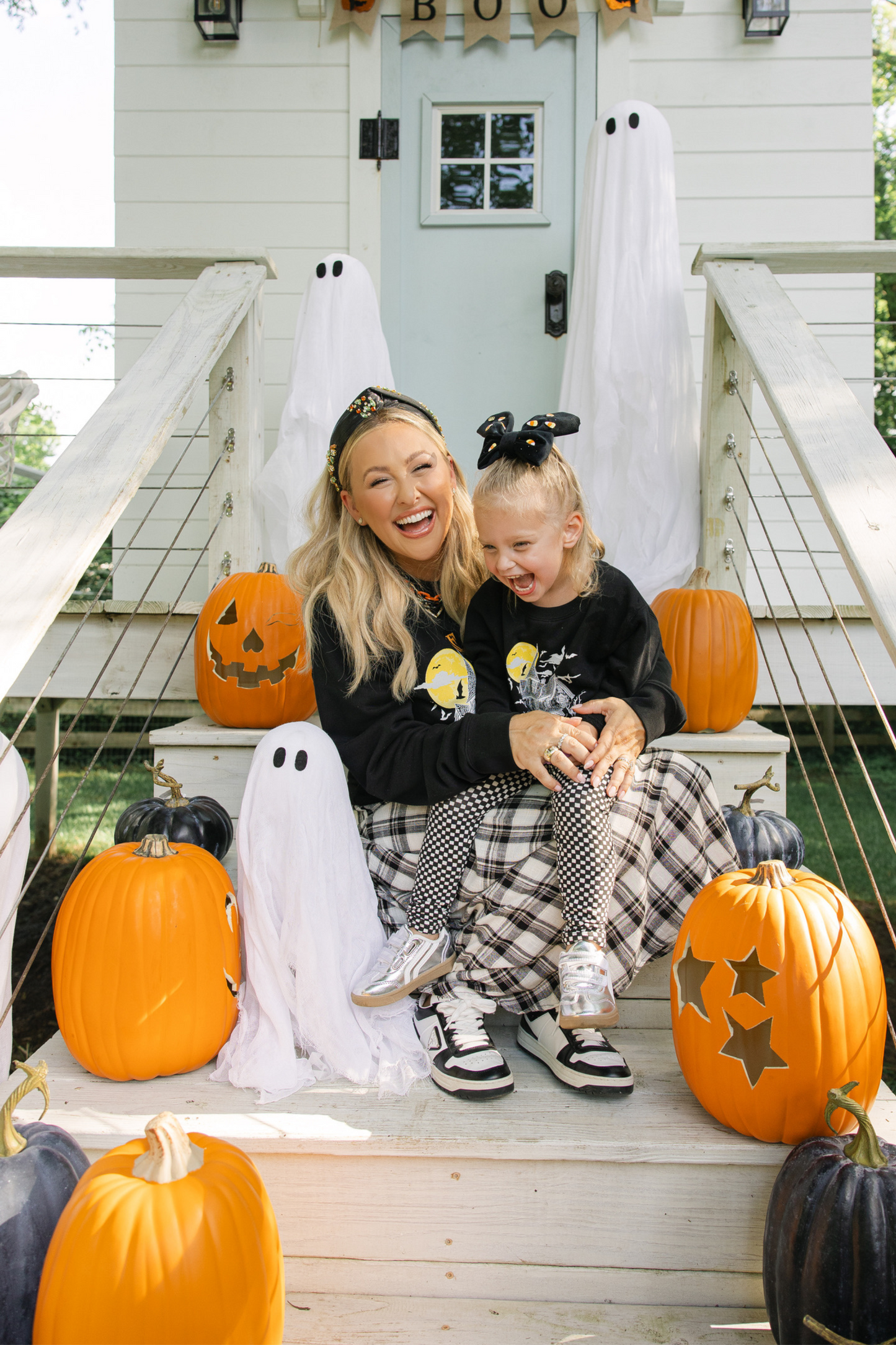 Woman and child sitting on a Halloween-themed playhouse with pumpkins and ghosts.