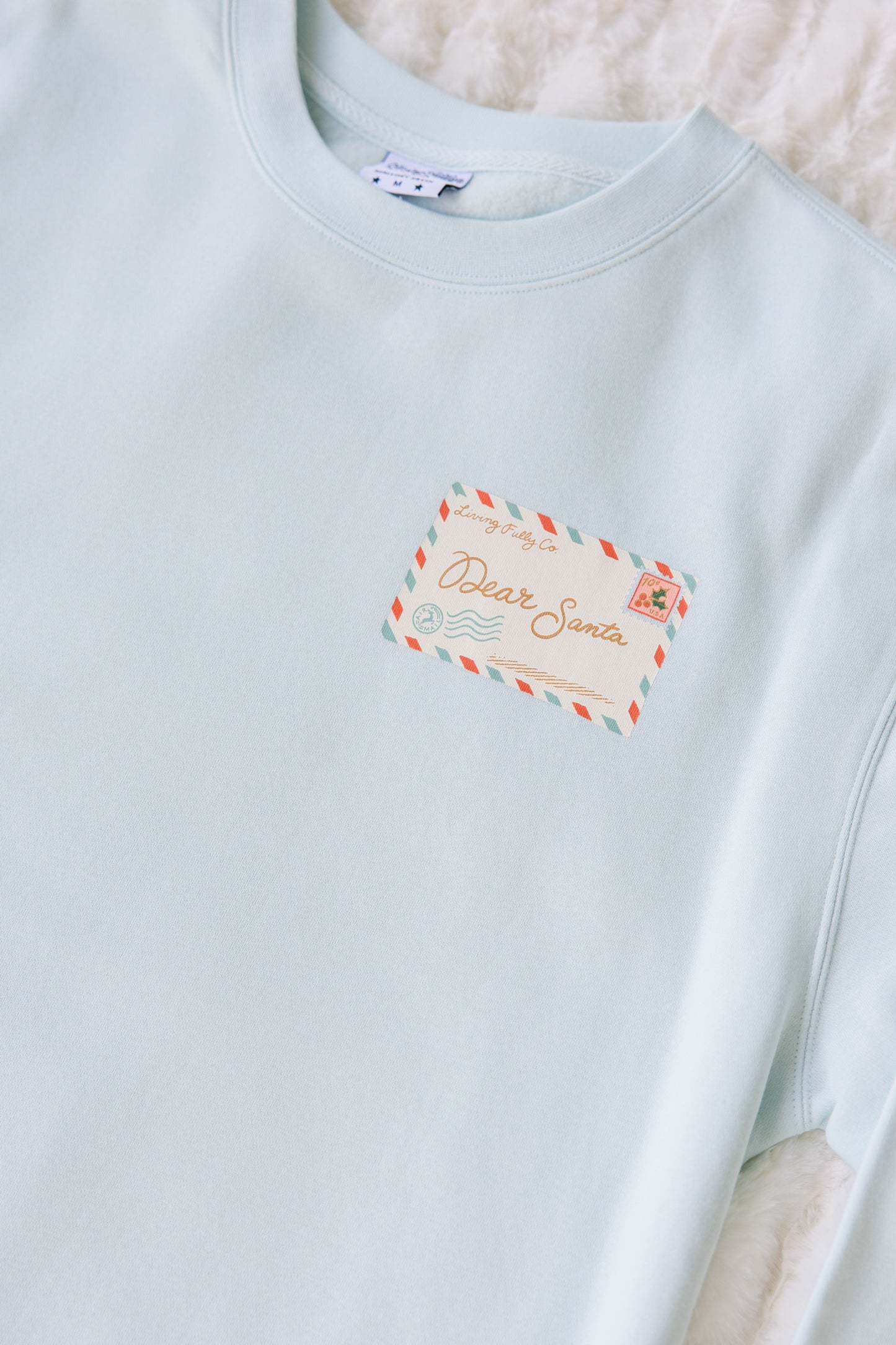 Light blue sweatshirt with a decorative label on a textured surface