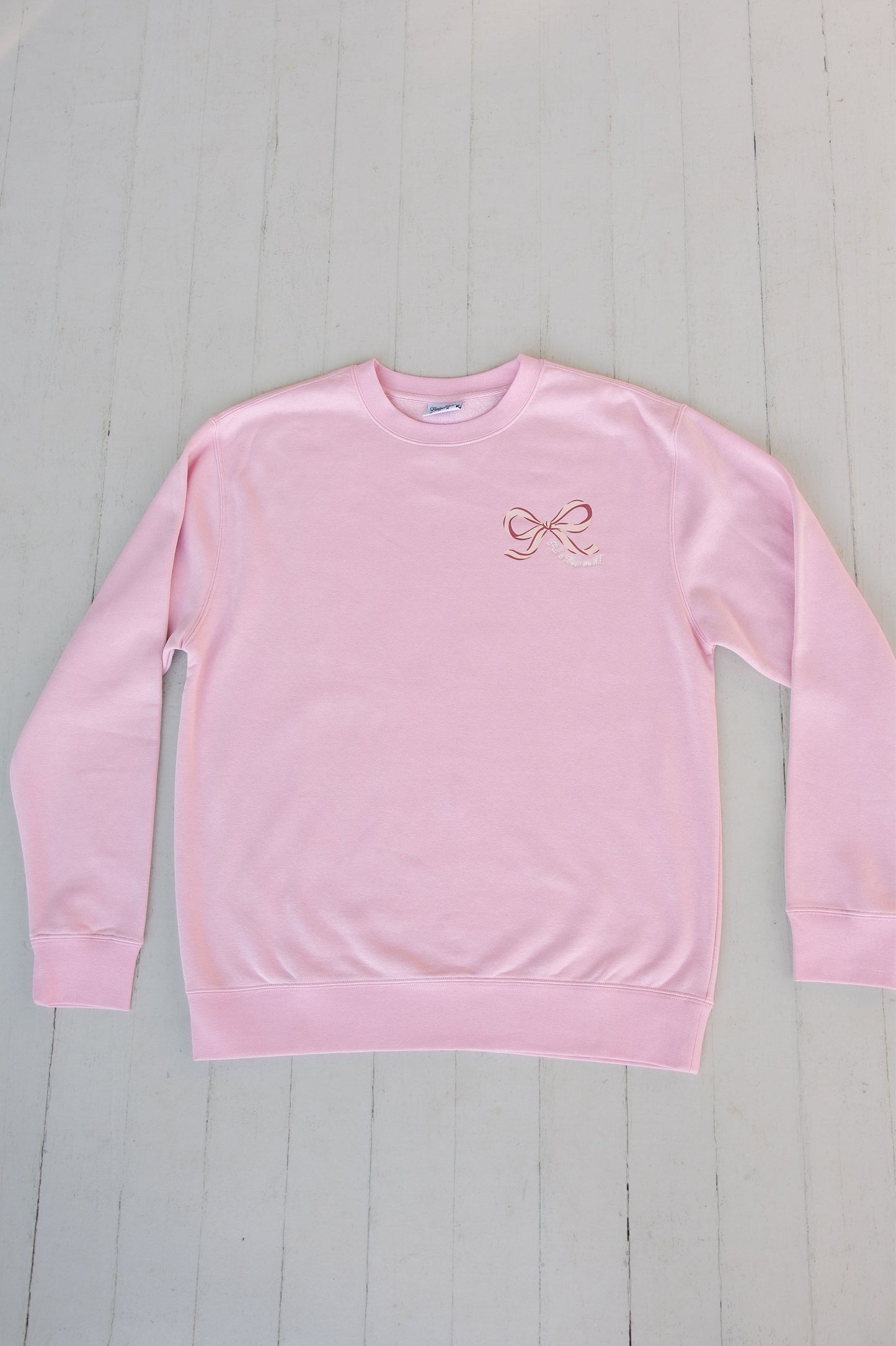 Pink sweatshirt with a logo on a light gray wooden surface