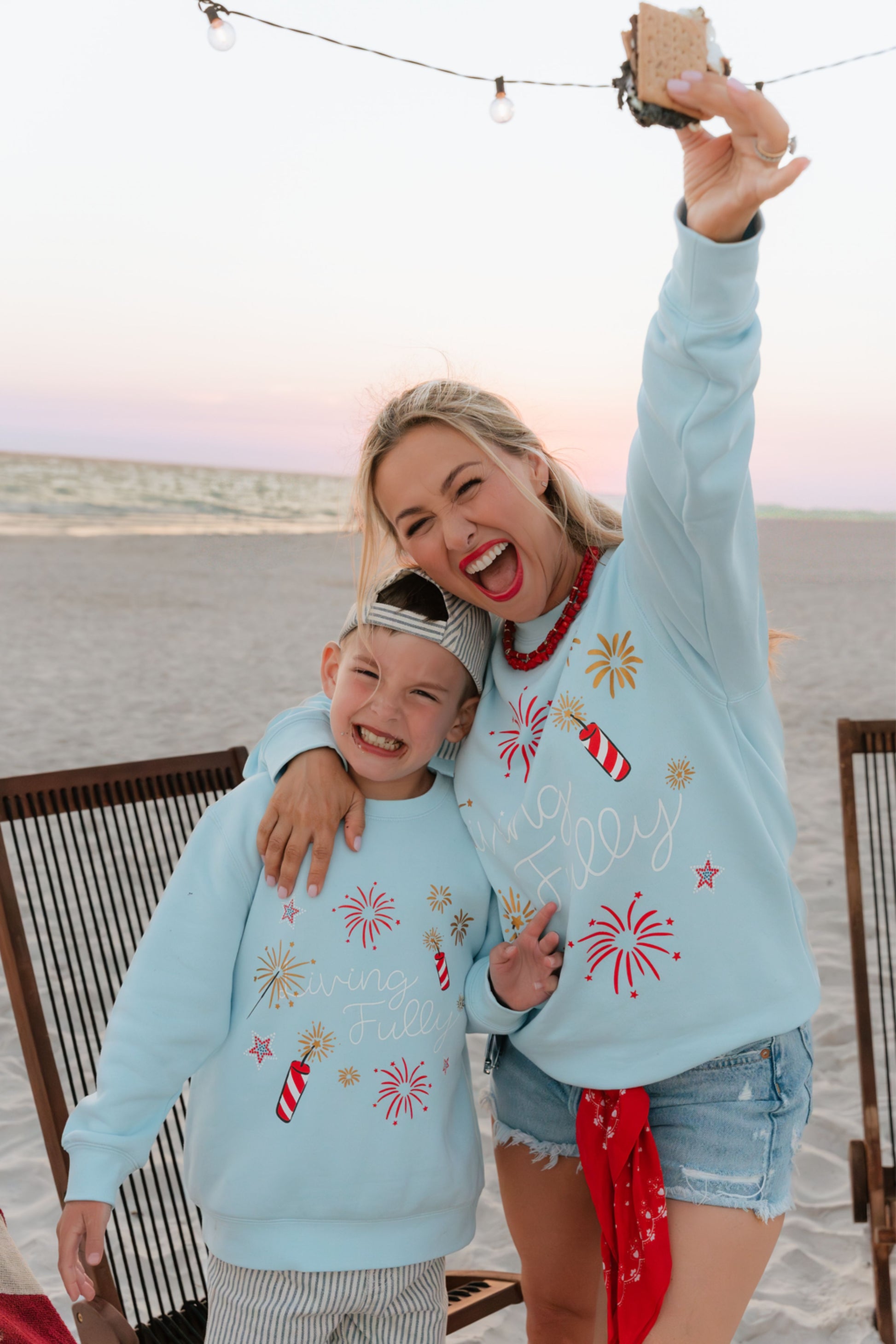 woman on beach at bonfire wearing light blue firework sweatshirt 