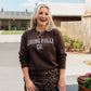 A woman stands outdoors wearing a dark brown sweatshirt with 'LIVING FULLY CO.' printed in white across the chest, paired with a leopard-print skirt.