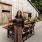 A woman stands outdoors in front of a rustic barn, wearing a dark brown sweatshirt with 'LIVING FULLY GO.' printed in white across the chest and a long brown plaid maxi skirt.