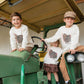 Three children wearing matching cream long-sleeve shirts with a brown turkey graphic, posed on a vintage green tractor inside a barn.