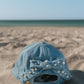 Blue denim cap with pearl embellishments on a sandy beach
