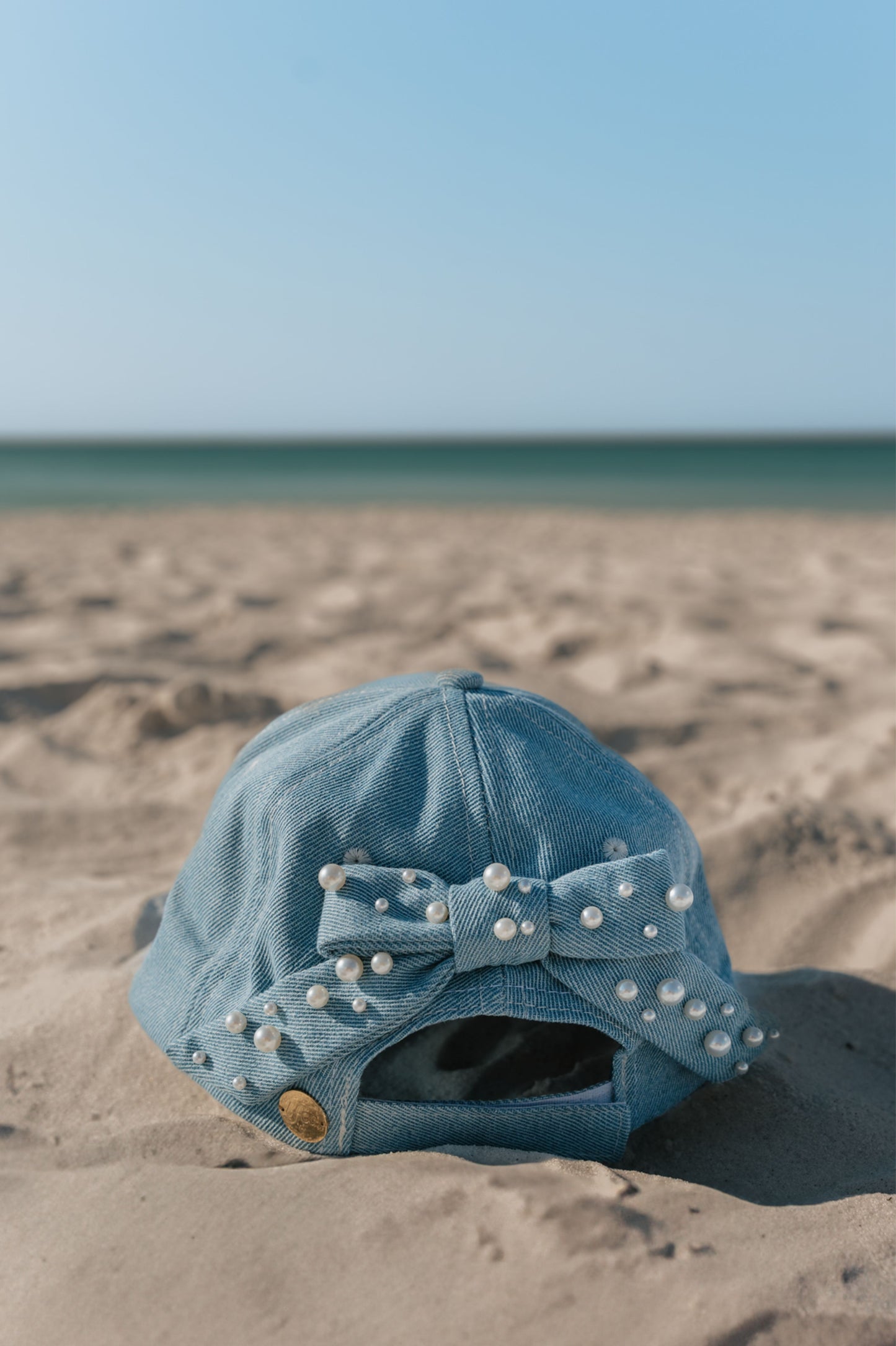 Blue denim cap with pearl embellishments on a sandy beach