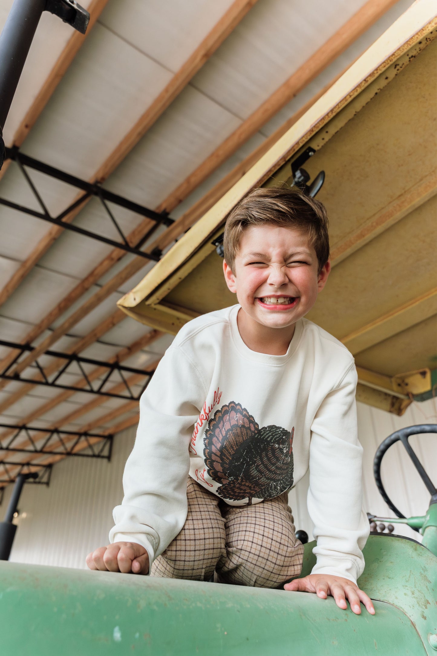 kid wearing turkey sweatshirt smiling on tractor
