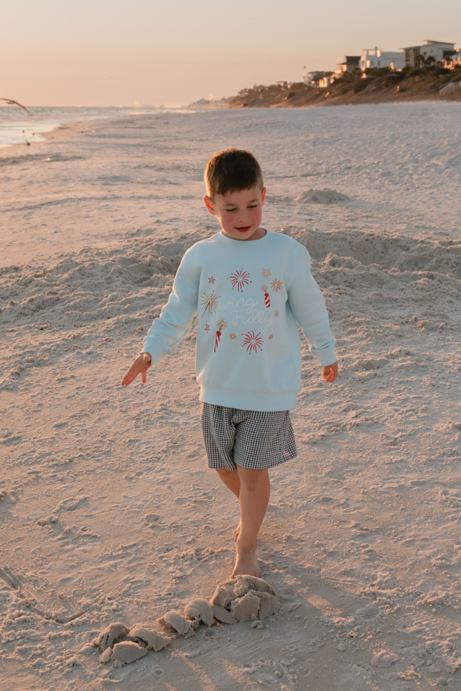 boy on beach wearing light blue sweatshirt and shorts 