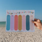 Hand holding a colorful calendar with 'the good ol' days are today' text against a beach background.