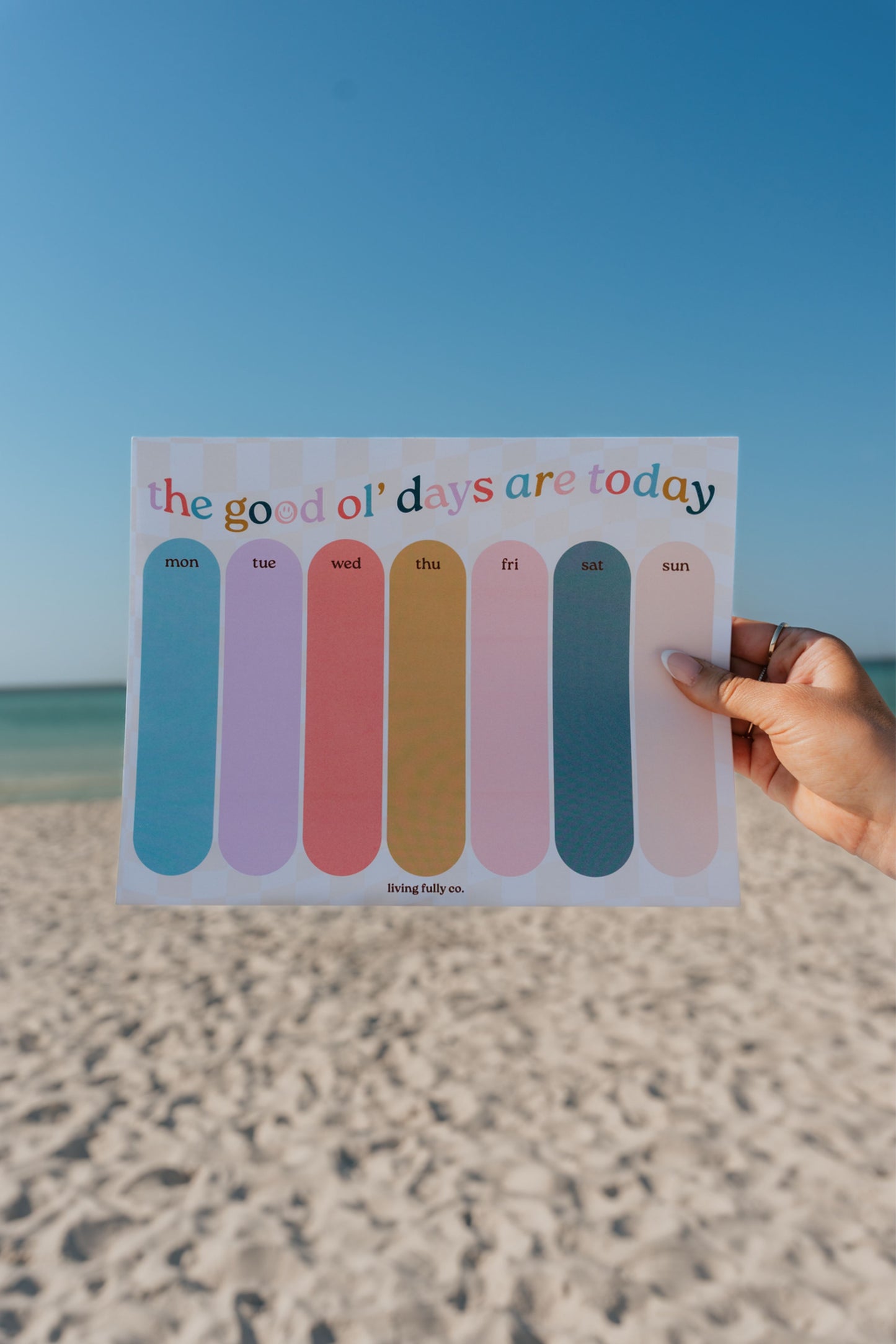 Hand holding a colorful calendar with 'the good ol' days are today' text against a beach background.