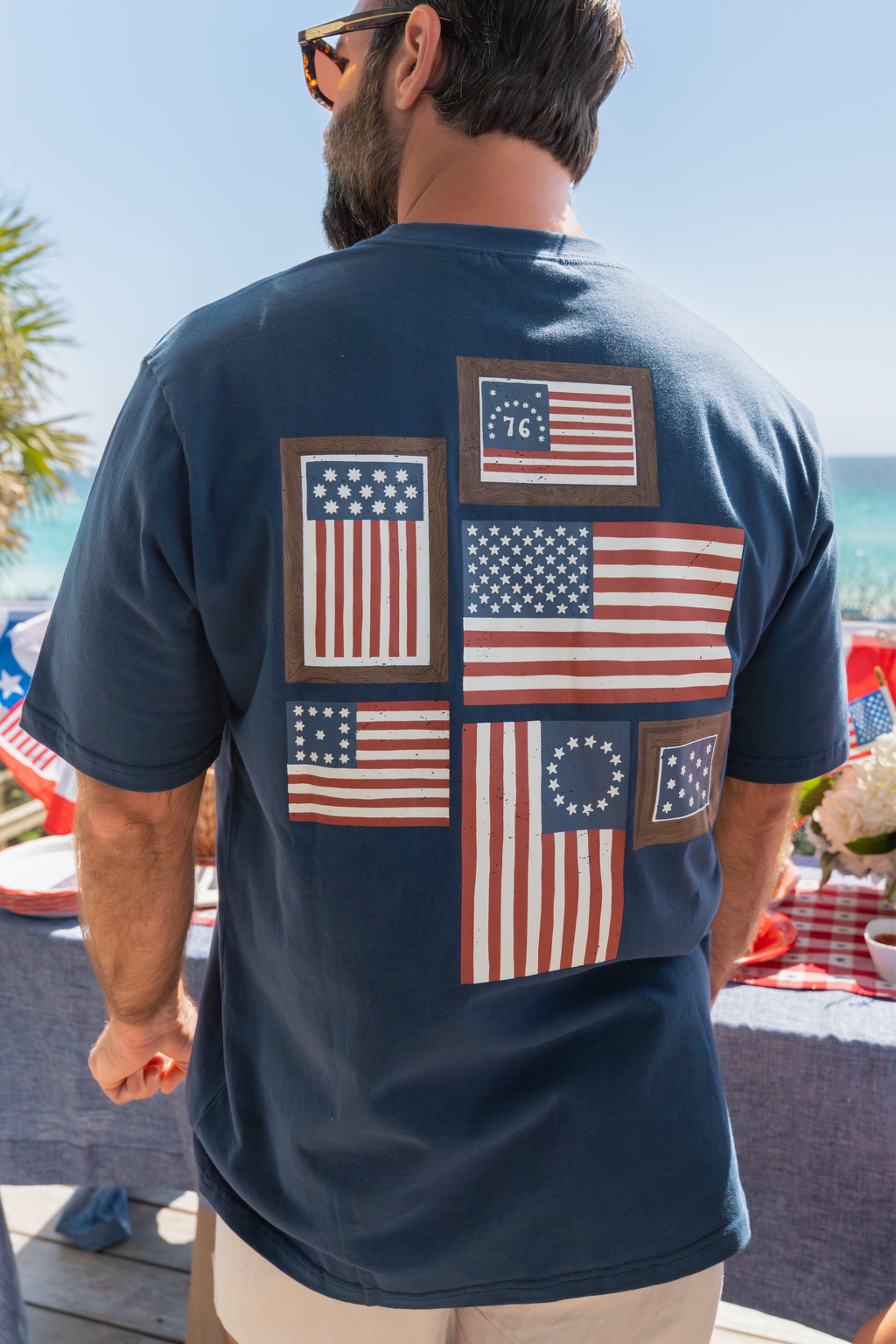 Man wearing a navy blue t-shirt with American flag designs on the beach.