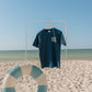 Navy blue t-shirt with 'USA' text on a white stand against a beach backdrop