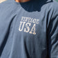 Navy blue t-shirt with 'Vintage USA' text worn by a person against a light blue background