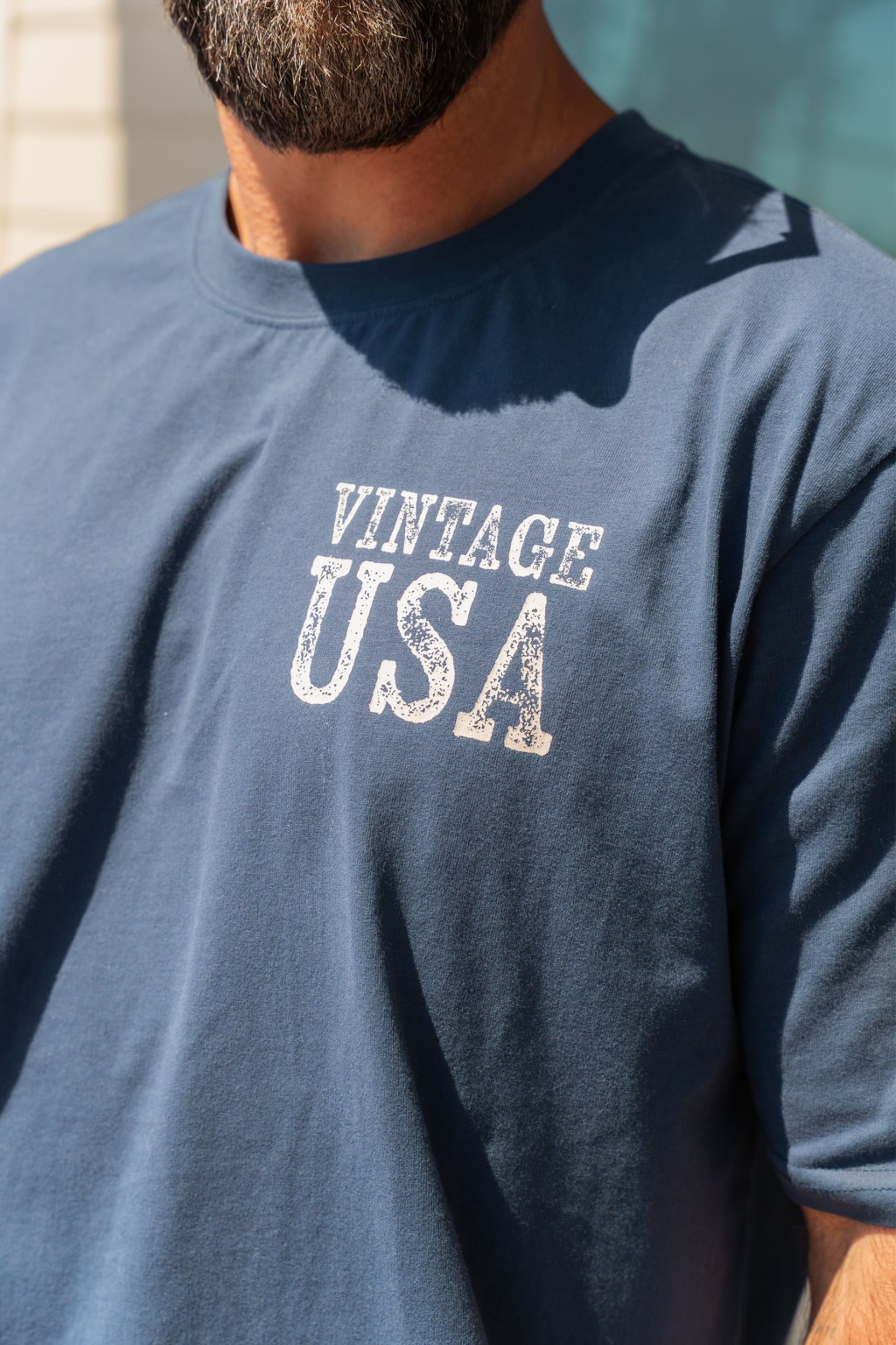 Navy blue t-shirt with 'Vintage USA' text worn by a person against a light blue background