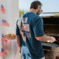 Man grilling outdoors with a decorative tee featuring American flags in the background