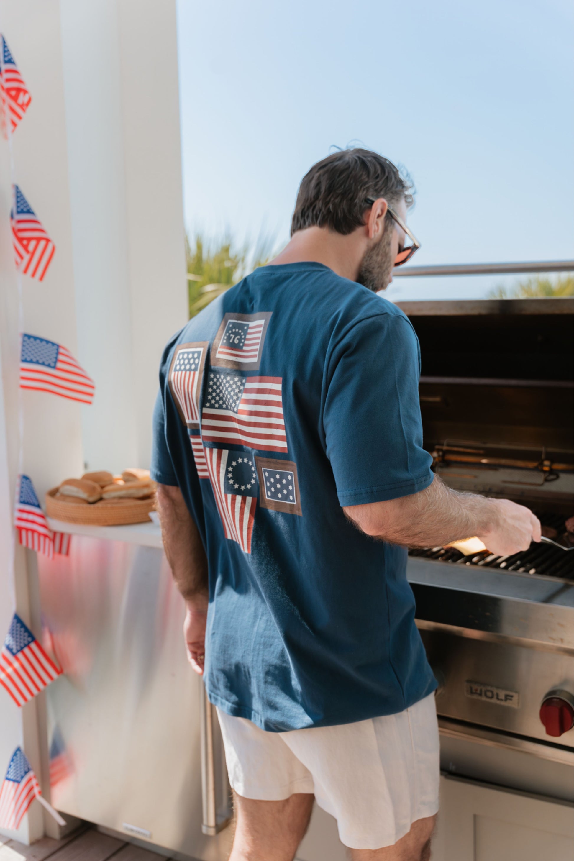 Man grilling outdoors with a decorative tee featuring American flags in the background