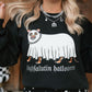 A woman wearing a black crewneck sweatshirt with a graphic of a white ghostly cat with orange paws and the text 'highfalutin halloween', paired with a black and white polka dot skirt.