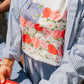 Person wearing a floral apron over a striped shirt, holding a red container.