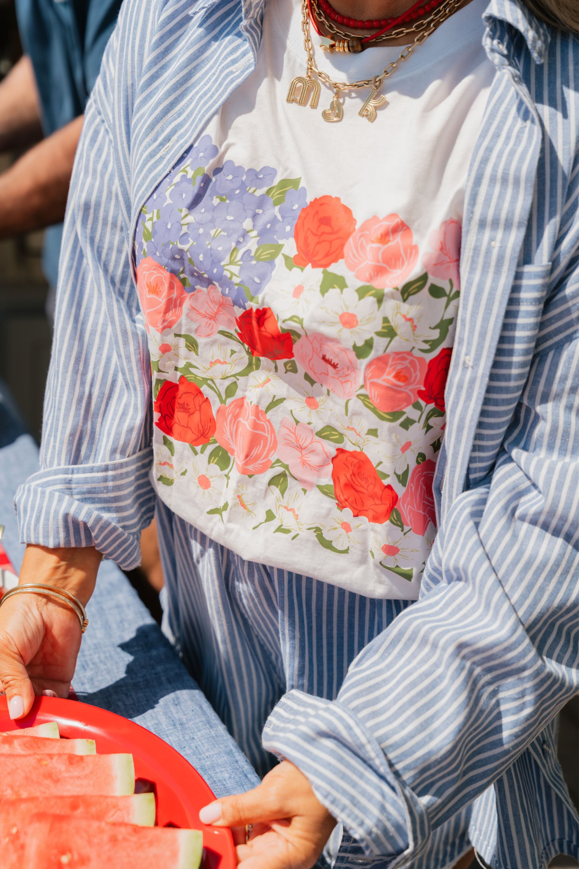 Person wearing a floral apron over a striped shirt, holding a red container.