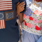 Person wearing a navy shirt with American flag patches and another person in a floral top and striped shorts.