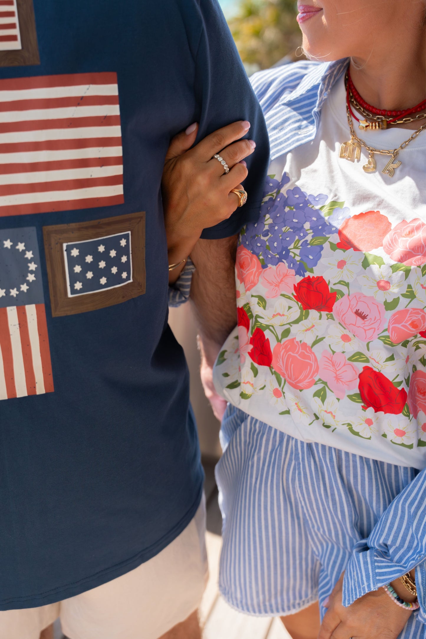 Person wearing a navy shirt with American flag patches and another person in a floral top and striped shorts.