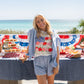 Woman standing by a table with a patriotic setup on a beach.