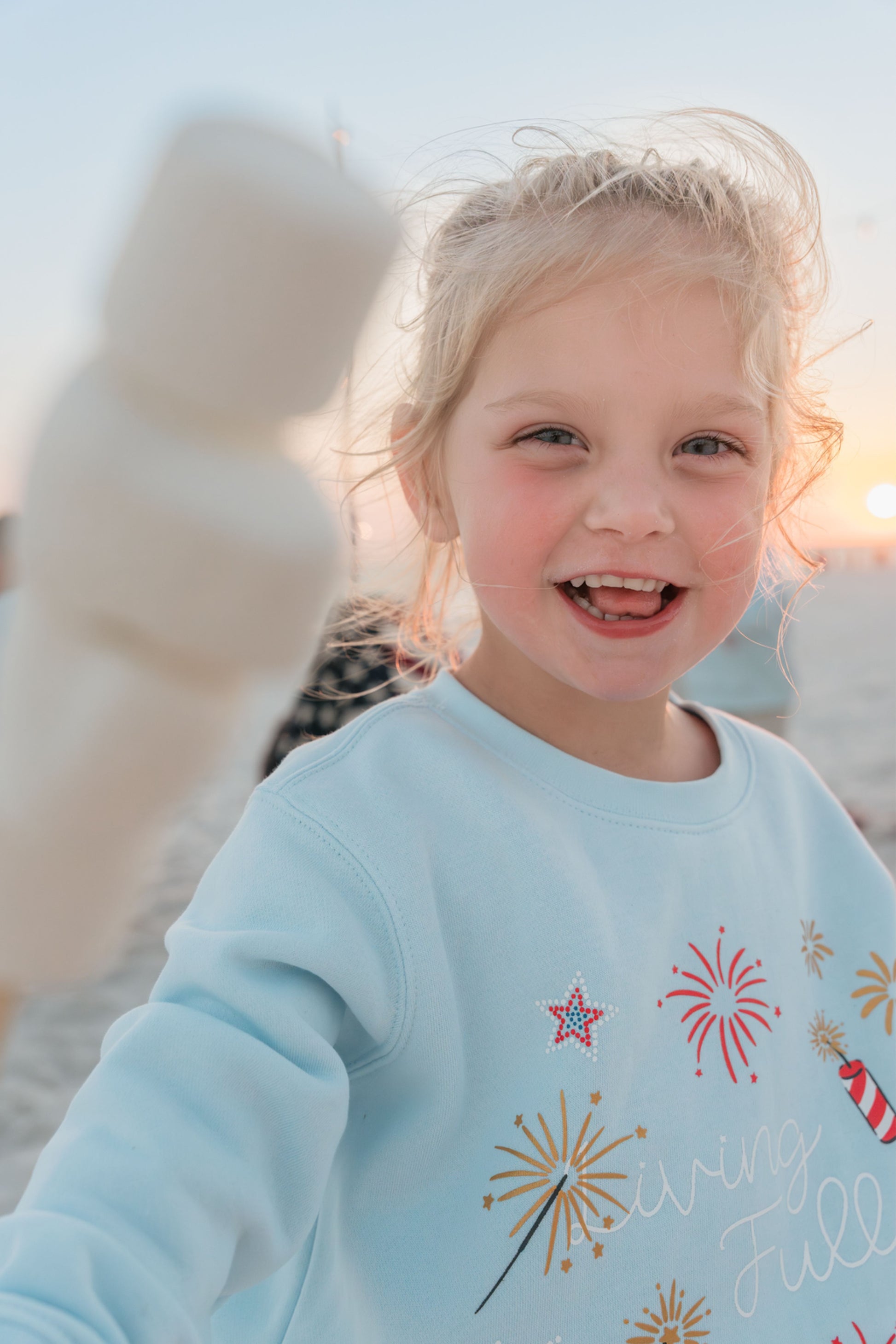 little girl with marshmallows wearing sweatshirt on beach 