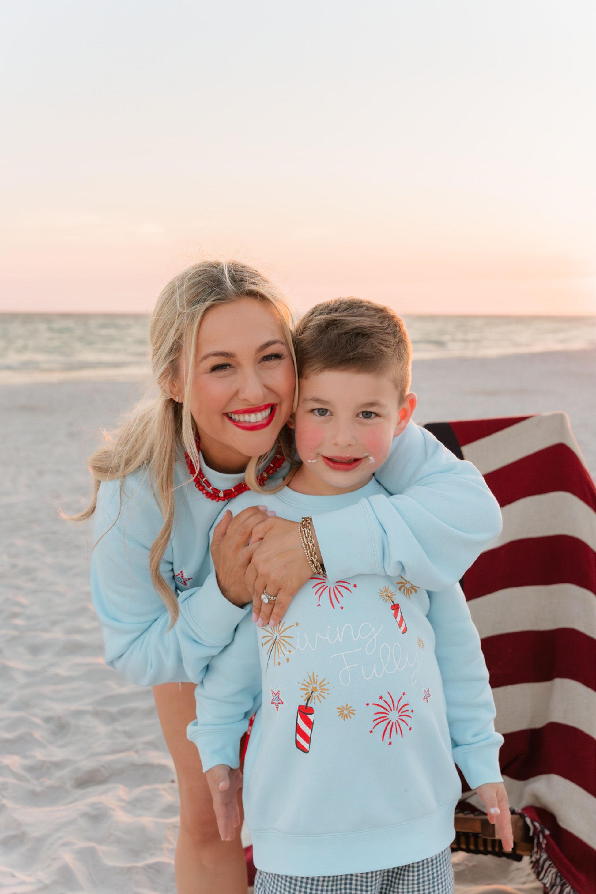 woman and kids on beach at bonfire wearing light blue firework sweatshirt 