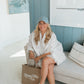 Woman sitting on a couch wearing a white shirt and blue cap, with a 'Living fully co' bag.
