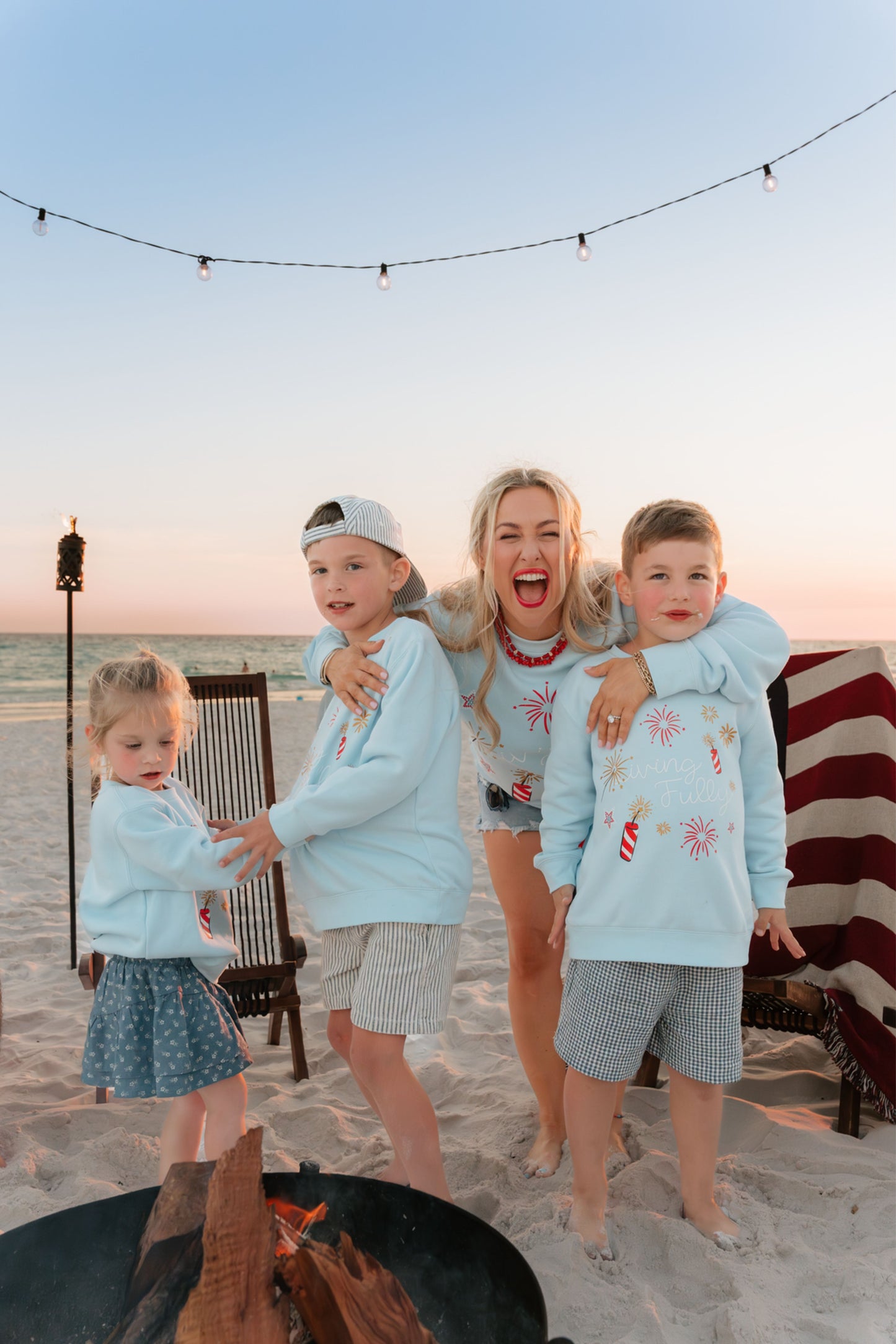woman  and kids on beach at bonfire wearing light blue firework sweatshirt 