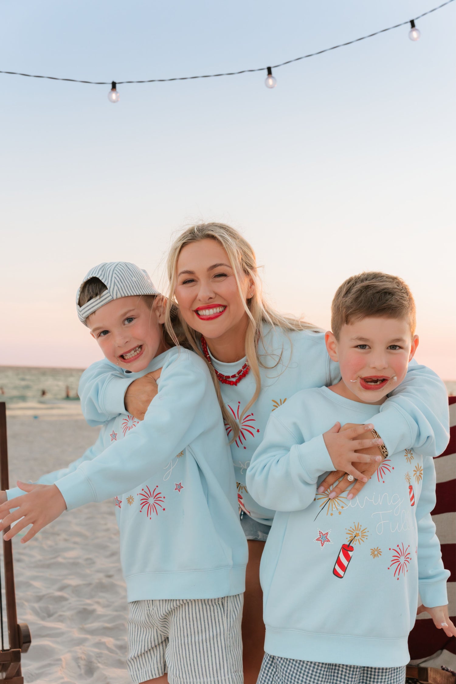 woman and kids on beach at bonfire wearing light blue firework sweatshirt 