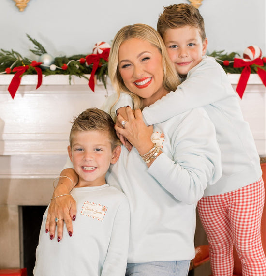 Woman and two children in matching outfits in front of a decorated fireplace with Christmas decorations.