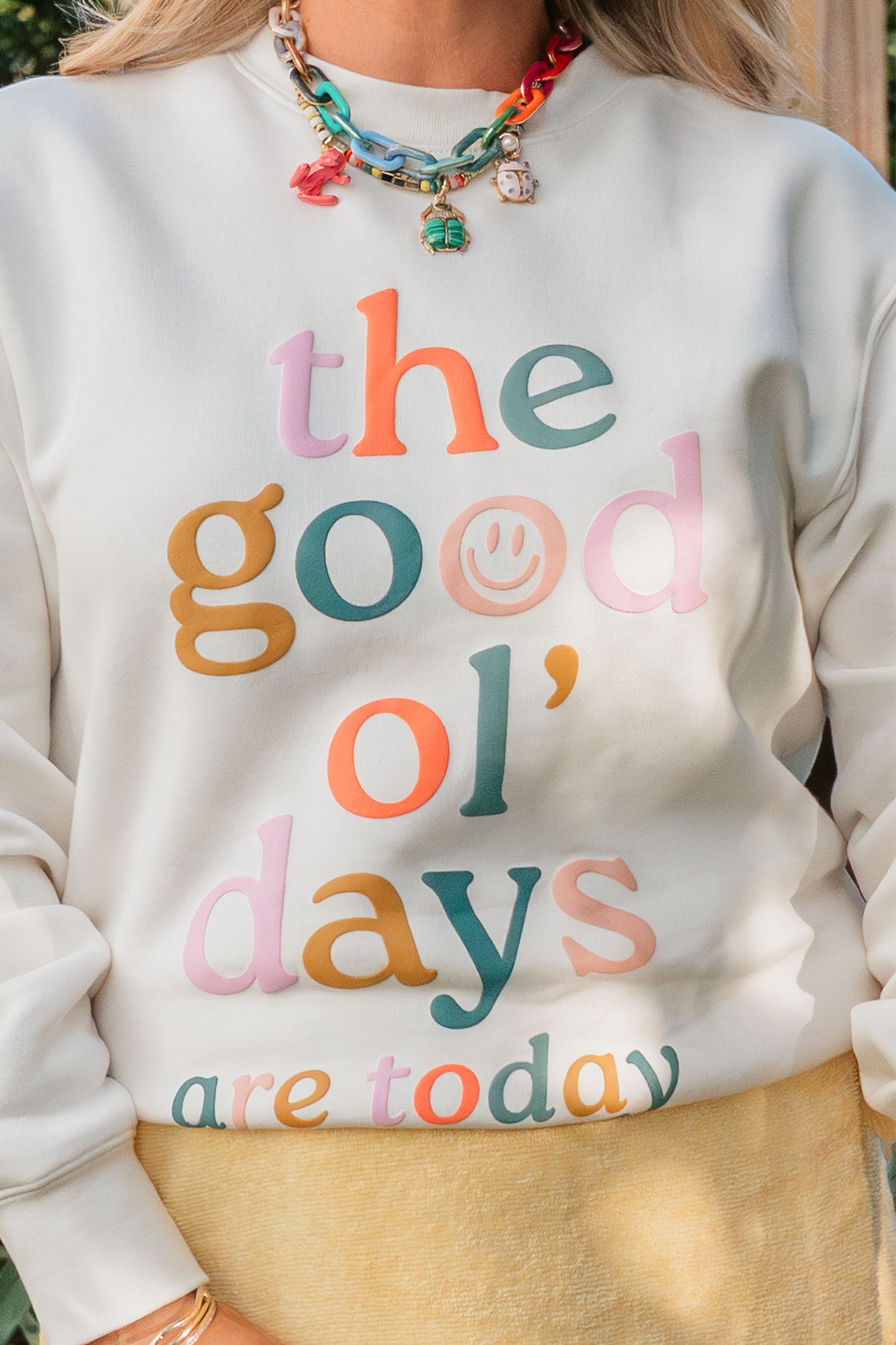 White sweatshirt with colorful text 'the good ol' days are today' worn by a person.