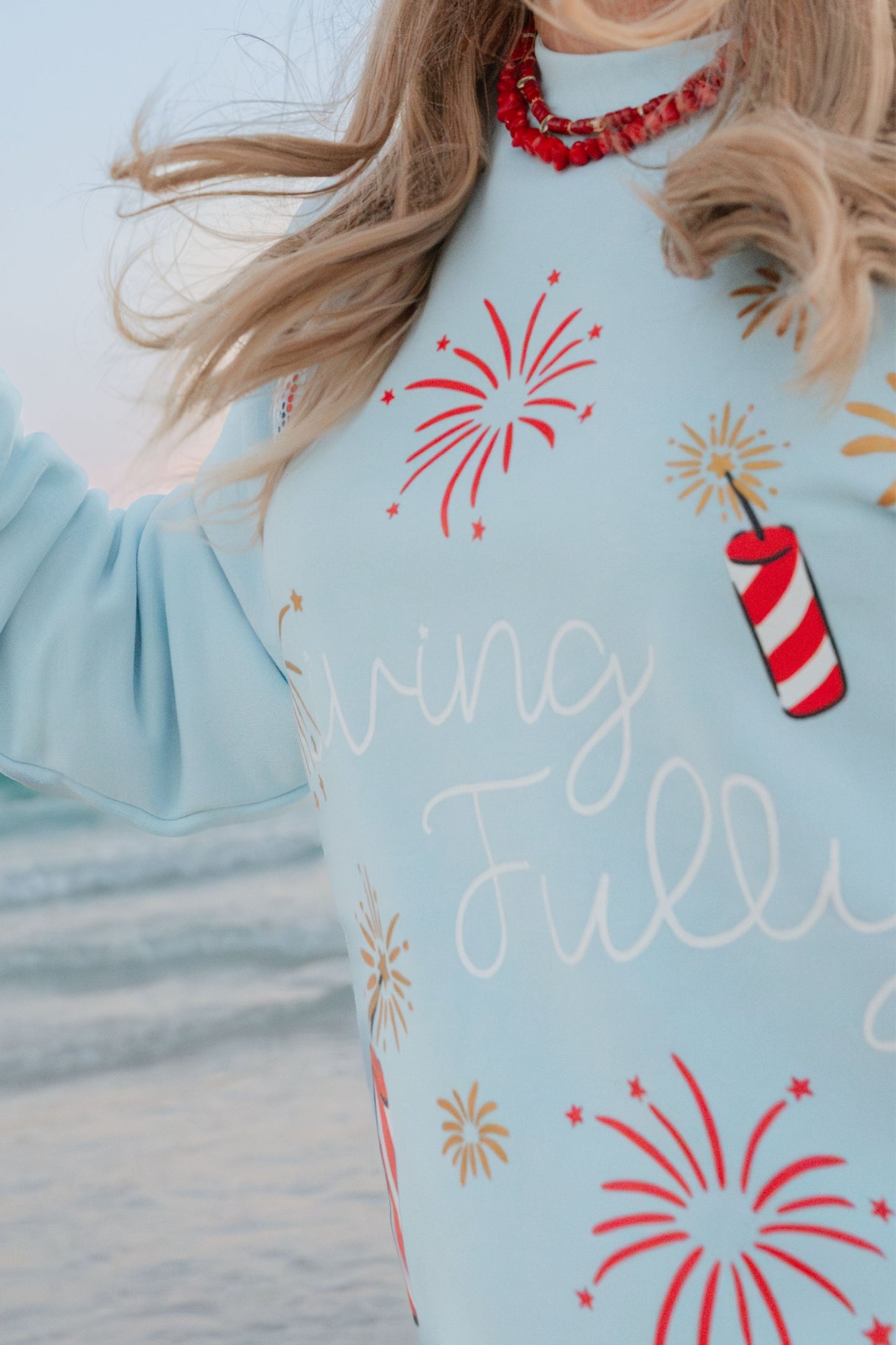 Light blue sweatshirt with red and gold firework designs and 'Living Fully' text.