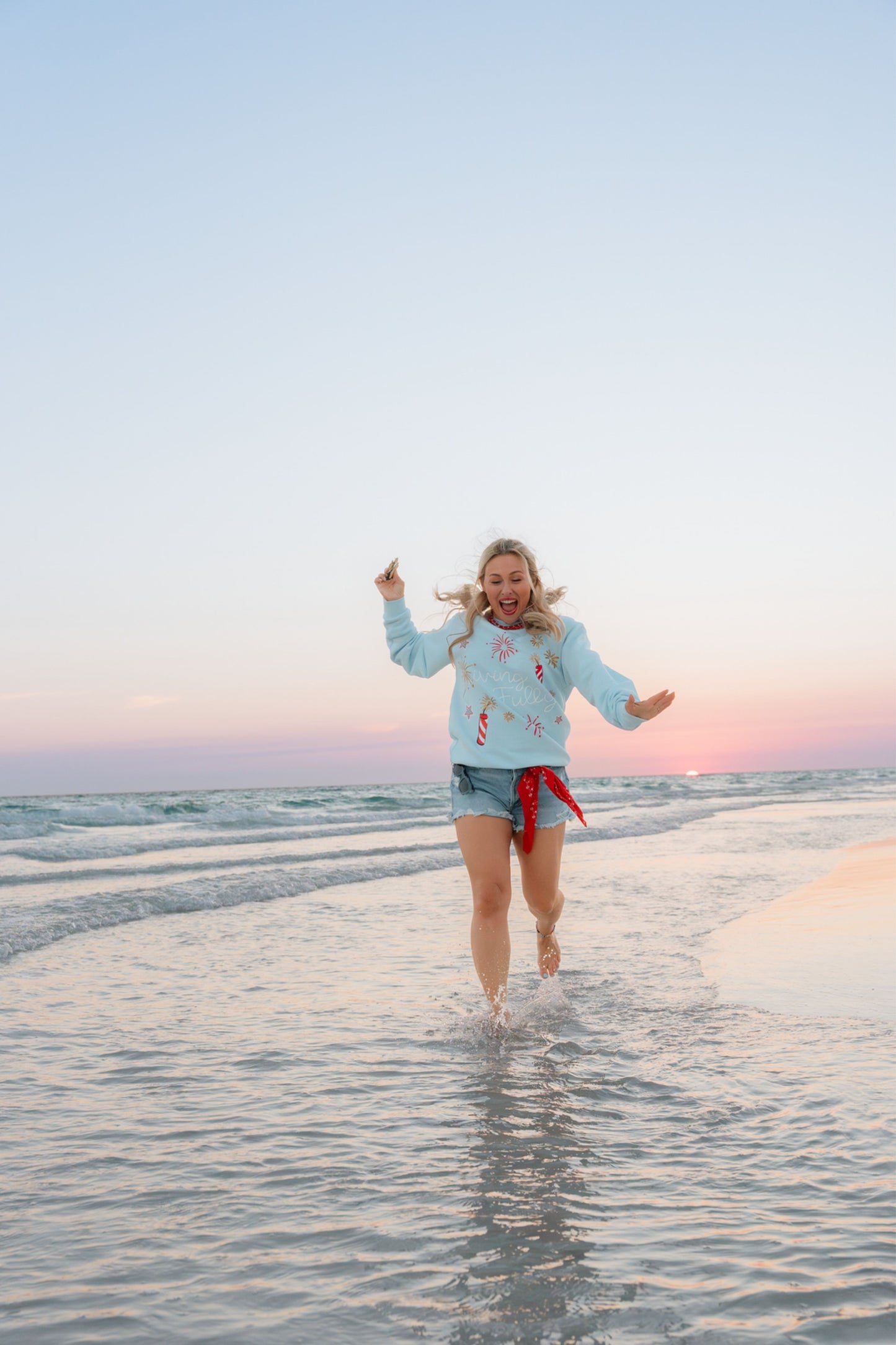 Person running on a beach with a colorful scarf belt and Living Fully Sweatshirt.