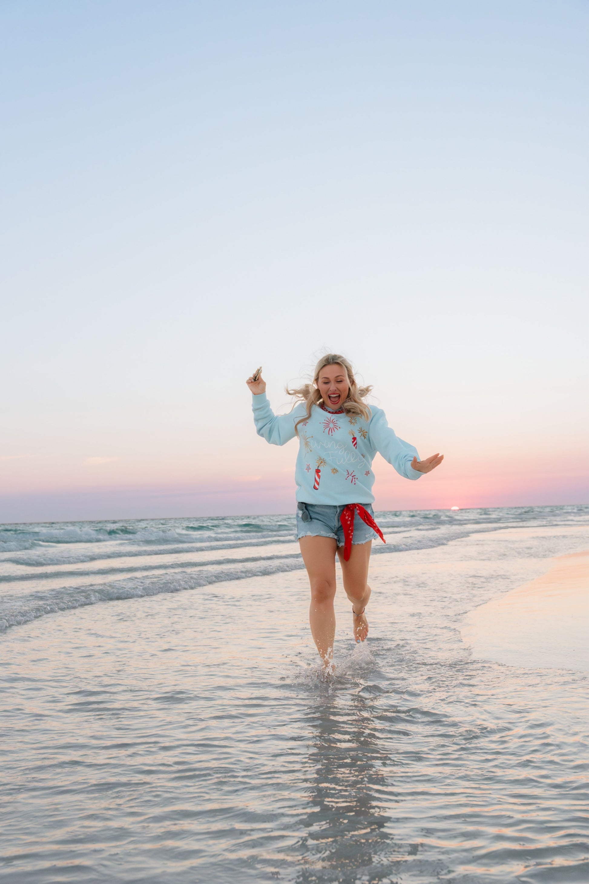Person running on a beach with a colorful scarf belt and Living Fully Sweatshirt.