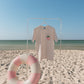 T-shirt with a strawberry design on a stand next to a life buoy on a sandy beach.