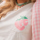 Person wearing a light pink shirt with a pink strawberry graphic and 'FC' text, paired with a pink checkered sleeve.