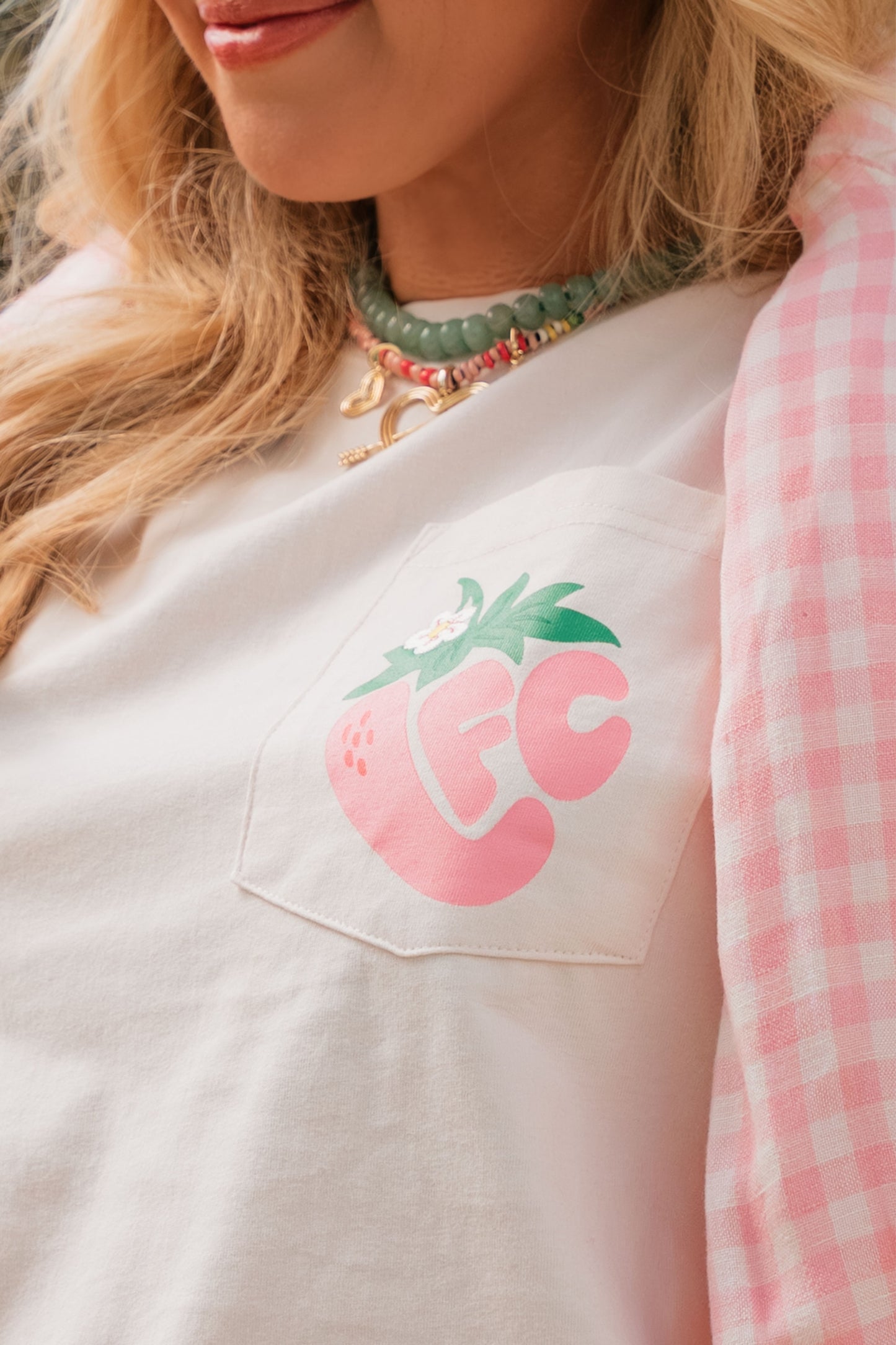 Person wearing a light pink shirt with a pink strawberry graphic and 'FC' text, paired with a pink checkered sleeve.