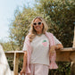Woman wearing a light pink t-shirt with a strawberry graphic, pink shorts, and a pink cardigan, standing outdoors.