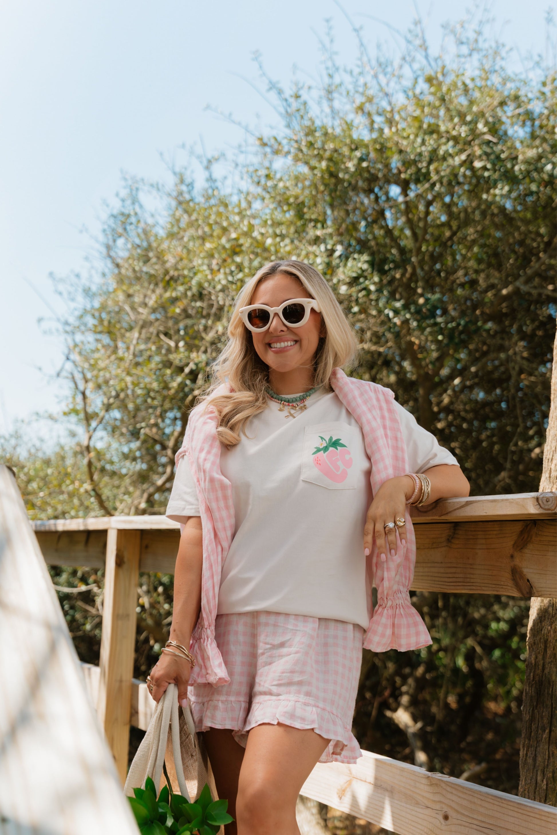 Woman wearing a light pink t-shirt with a strawberry graphic, pink shorts, and a pink cardigan, standing outdoors.