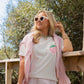 Woman wearing a pink t-shirt with a strawberry design, pink checkered jacket, and shorts outdoors.