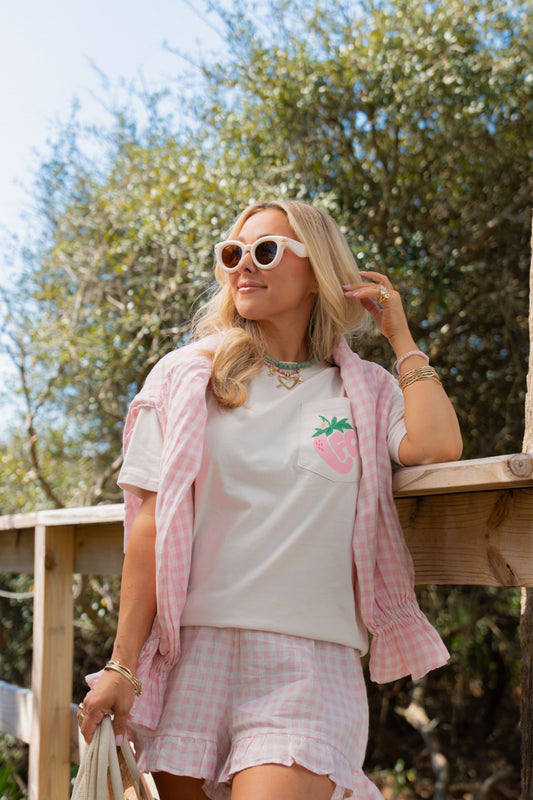 Woman wearing a pink t-shirt with a strawberry design, pink checkered jacket, and shorts outdoors.
